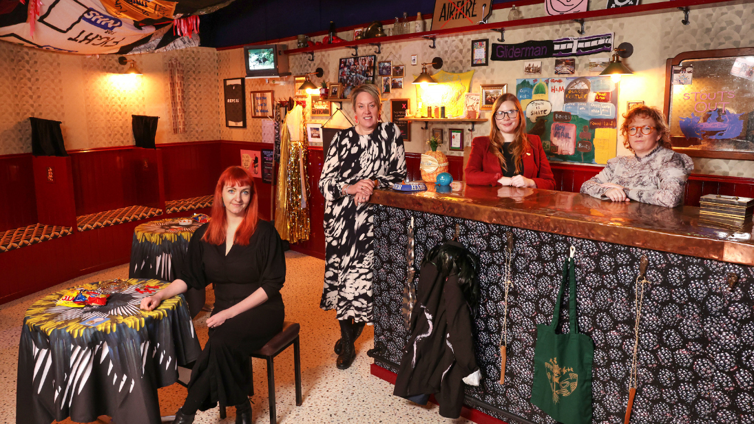 People standing inside Irish sibin containing objects, artwork, furnishings and a bar that is the 2021 Turner Prize and it's installed inside the Ulster Museum