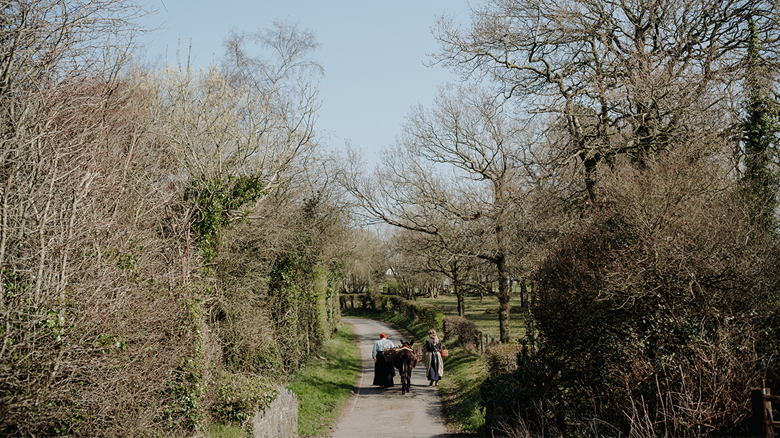 Two women in old fashioned clothing walking with a donkey in the countryside