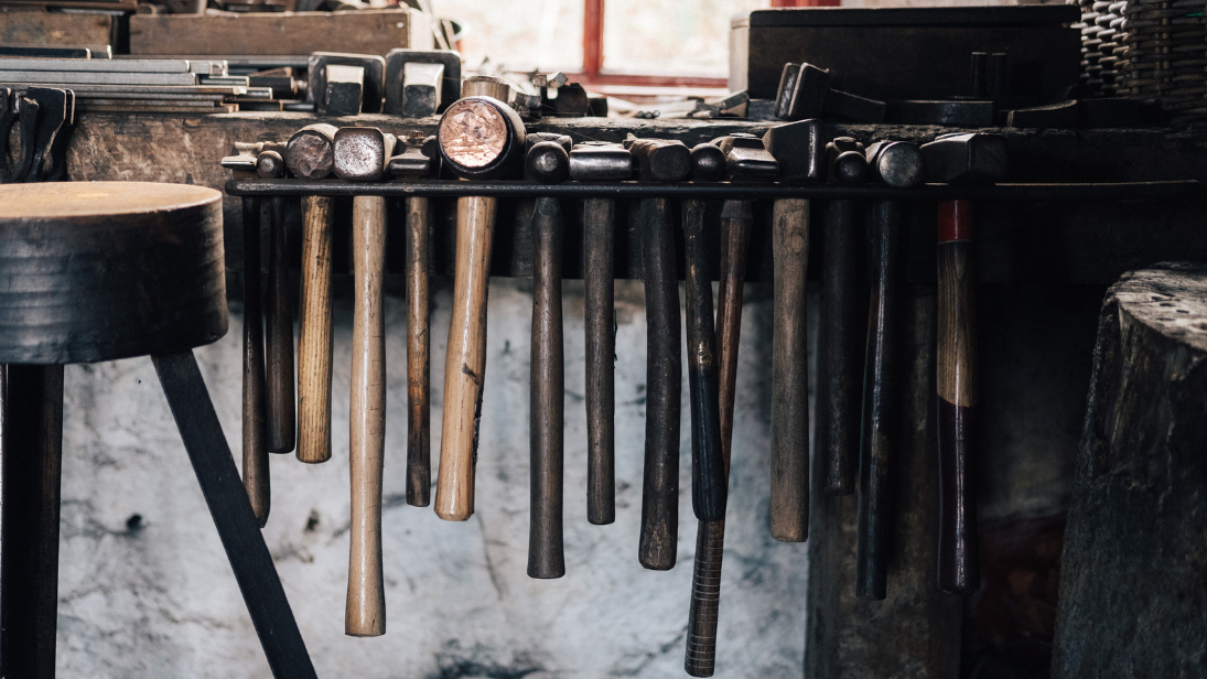 A bunch of hammers dangle in a row on a bench.