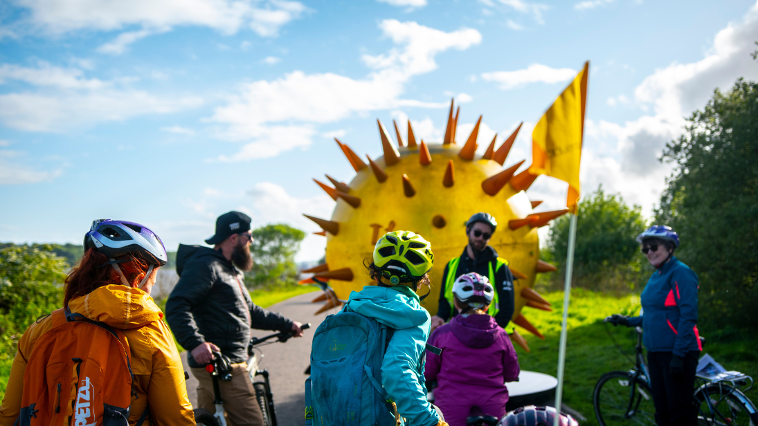 six people on bikes in front of a planet art sculpture