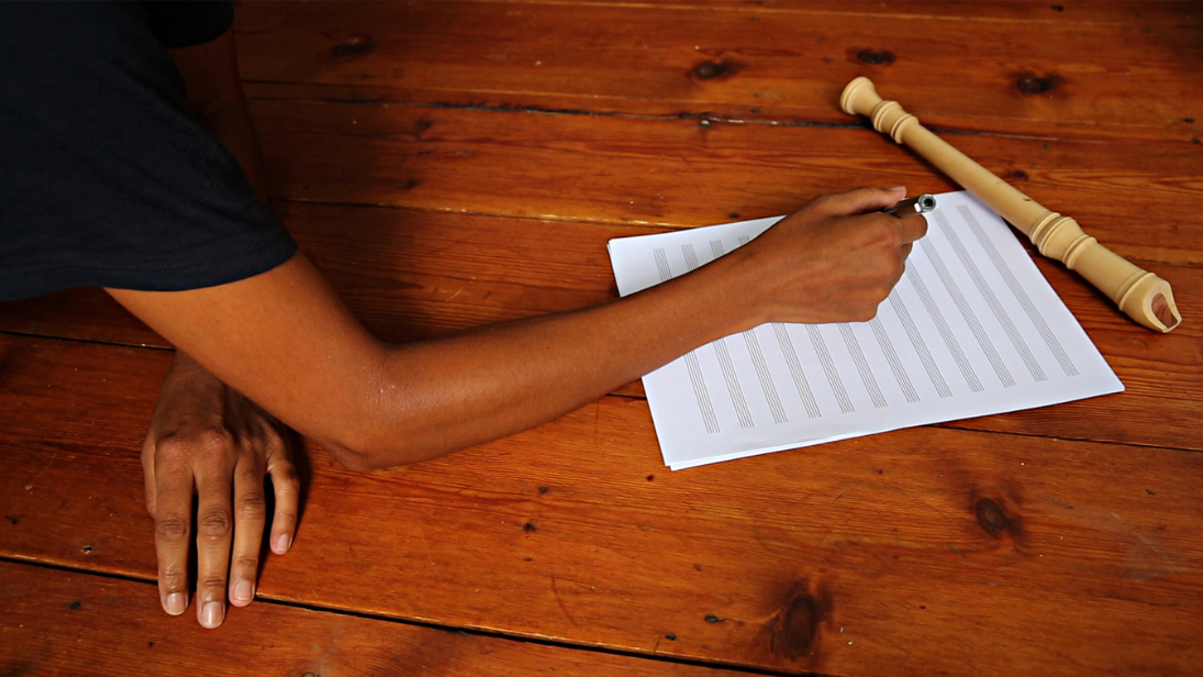 the arm of a person writing on sheet music 