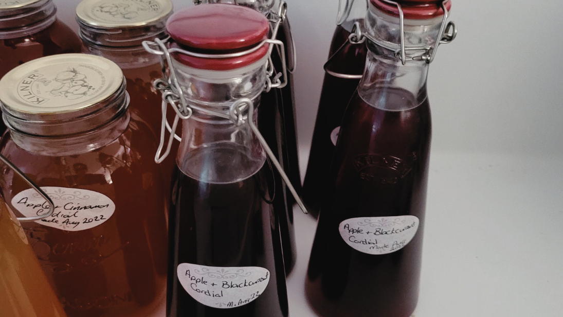 Glass jars some with gold lids, others with red lids, with handwritten labels for cordial flavours.