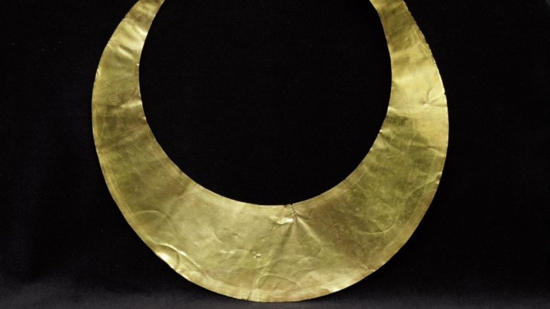 a gold circular necklace on a black background