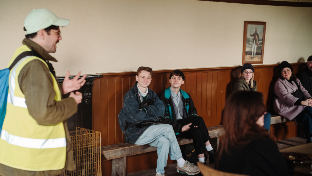 Event organiser addressing room with people sitting on benches