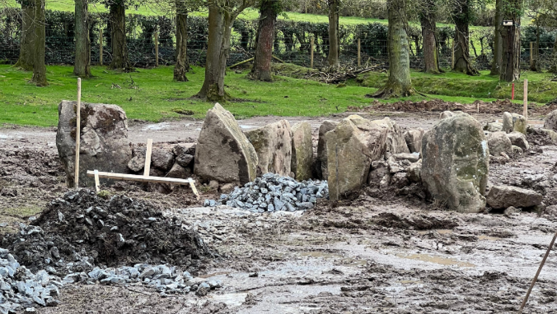 A muddy field has been excavated and large stones are buried in the ground.