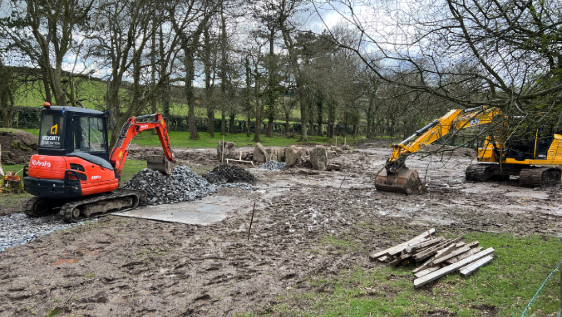 Two diggers in a field are excavating ground.