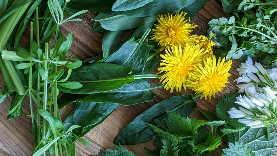 Foraged greens lie on a wooden cutting board.