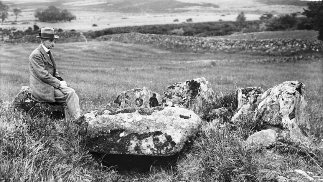 A man sits on a stone overlooking an archaeological monument.