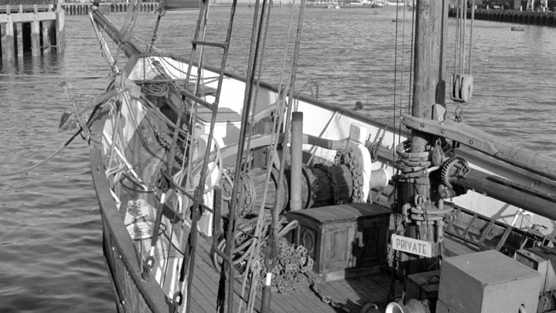 Black and white photograph, looking closely at the deck of the Result. Private sign hanging from the mast