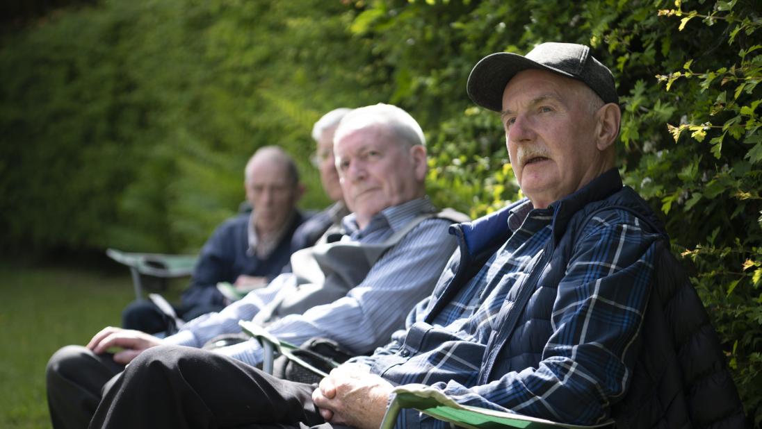 Four people sat by a hedge enjoying the festival