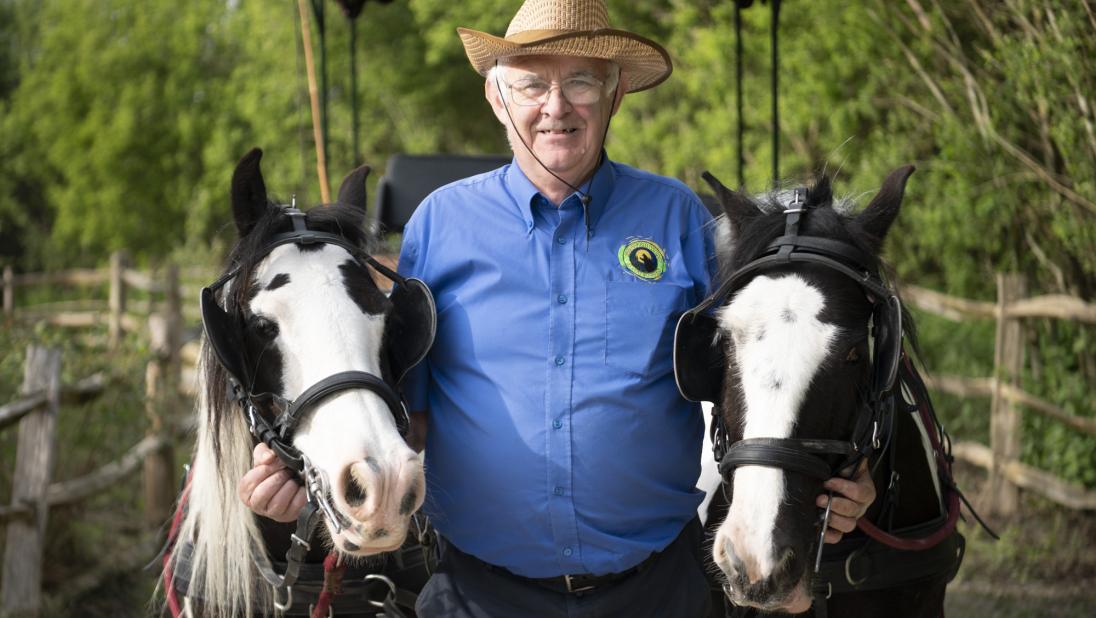 A man stood with two horses and a cart