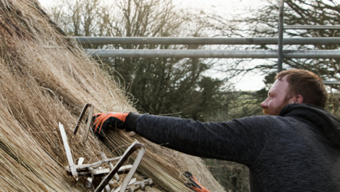 A man places a peg to hold new thatch in place.