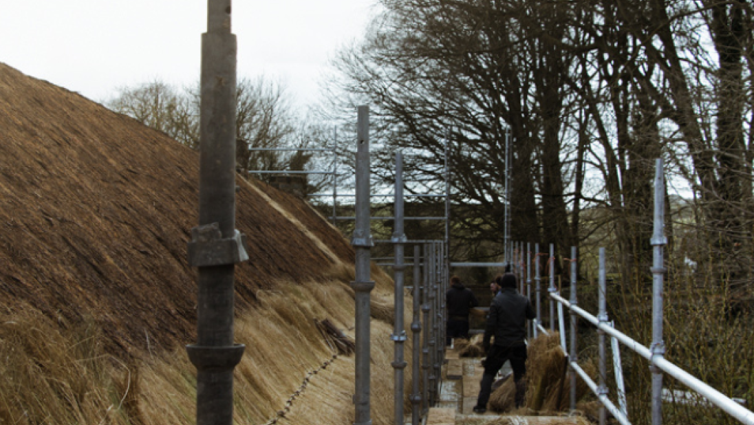 A view of a roof being thatched from up close on scaffolding.