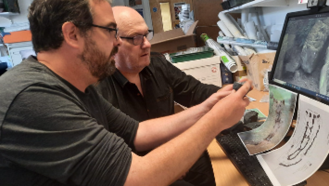 Two men study a computer rendering of a Neolithic court tomb