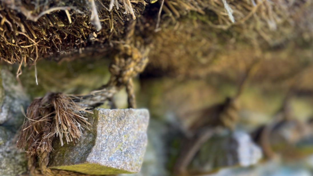 A close-up of a stone jamb in an outer cottage wall with thatch rope tied to it. 