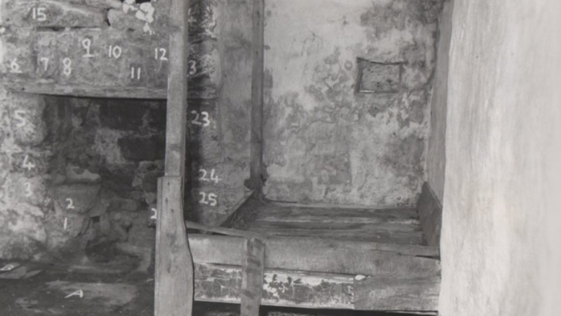 The inside of a run-down cottage. The stones of the walls are numbered with white chalk.