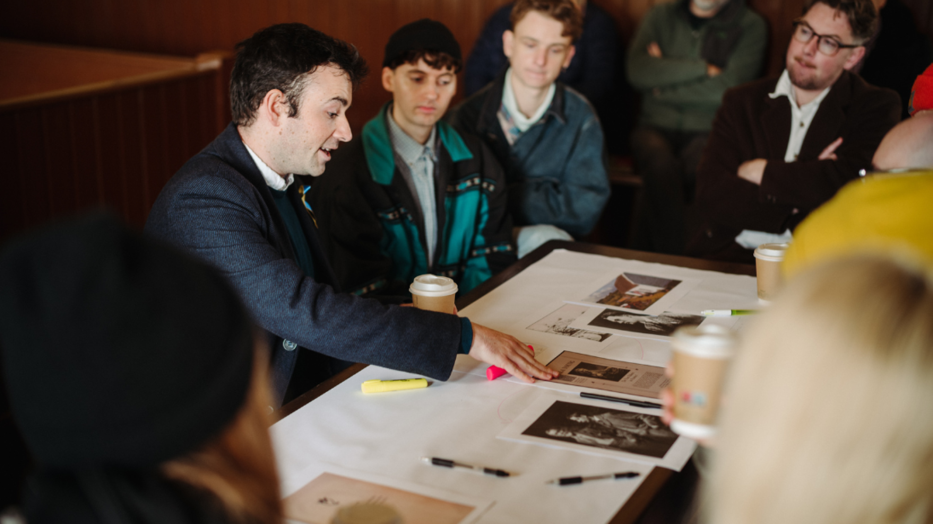 People gathered around a table with photos and paper spread on top and someone leading the conversation