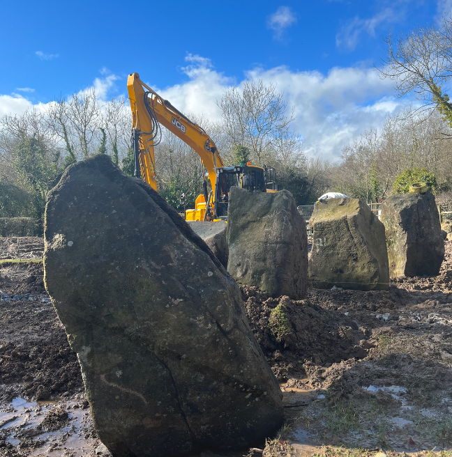 Standing stones in the foreground while in the background a yellow digger stands. 