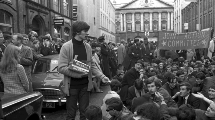 Voices of 68, black and white photograph of a young student giving things out to a crowd of other students