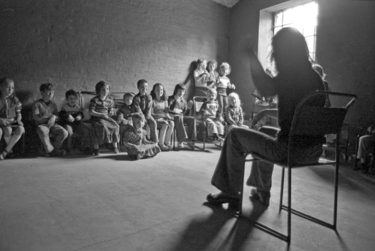 Teacher in the foreground talking and gesturing to children 