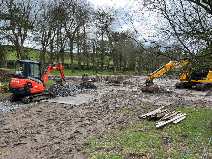 Two diggers in a field are excavating ground.