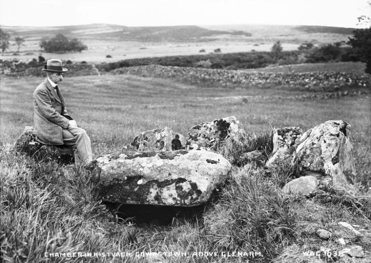 A man sits on a stone overlooking an archaeological monument.