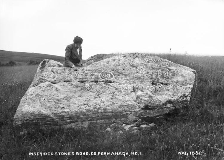 A woman sits on top of a large stone, carved with ancient symbols.