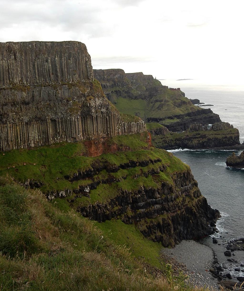 Cliffs east of the Giant’s Causeway. The dark Lower Basalt lava flows are capped by a weathered orange layer, and overlain by two lava flows with well-formed columns.