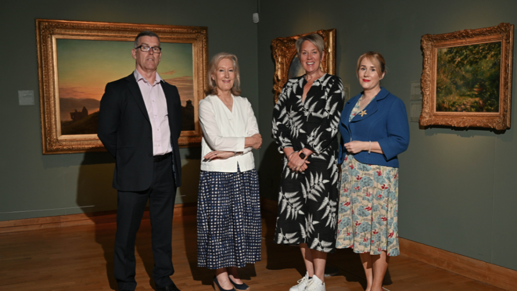Four people standing beside a Renoir painting on display in the Ulster Museum.